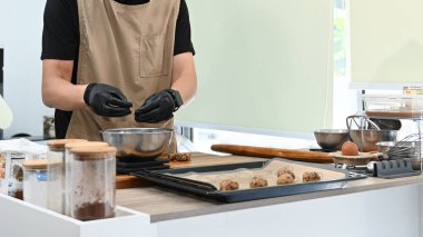 Bir adam kurabiye yapıyor ve eldiven giyiyor. Malzemeleri ölçmek için bir tartı kullanıyor. Kurabiyeler fırın tepsisinin üstünde...