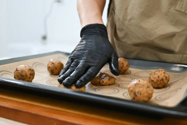 Bir adam kurabiye yapıyor ve eldiven giyiyor. Malzemeleri ölçmek için bir tartı kullanıyor. Kurabiyeler fırın tepsisinin üstünde...