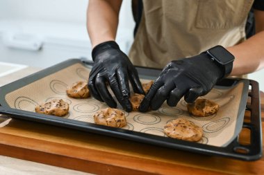 Bir adam kurabiye yapıyor ve eldiven giyiyor. Malzemeleri ölçmek için bir tartı kullanıyor. Kurabiyeler fırın tepsisinin üstünde...