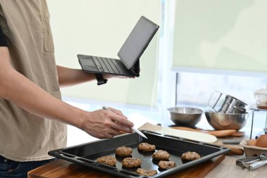 Bir adam elinde tablet tutarken mutfakta yemek pişiriyor. Tableti yemek tarifini bulmak için kullanıyor ya da yemek pişirme kursunu takip ediyor...