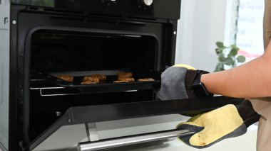 Bir insan fırından yemek çıkarıyor. Fırın siyah ve gümüş sapı var..