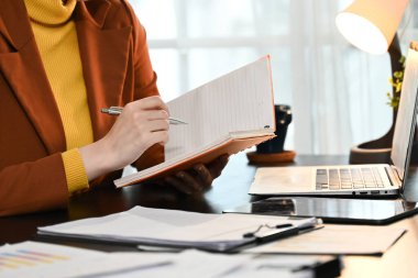 Bir kadın elinde defter ve kalemle masada oturuyor. Bir şeyler yazıyor ve işine odaklanmış durumda...