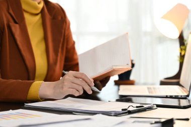 Bir kadın elinde defter ve kalemle masada oturuyor. Bir şeyler yazıyor ve işine odaklanmış durumda..