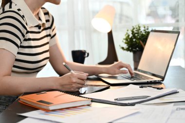 Masasında dizüstü bilgisayarı ve defteri olan bir kadın oturuyor..