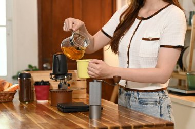 Bir kadın mutfakta çay yapıyor. Önlük takıyor ve elinde çay süzgeci tutuyor...