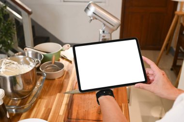 Bir insan mutfakta bir sürü kap kase ve kap olan bir tablet tutuyor. Tablet boş ve mutfak da birinin yemek hazırladığı bir yer gibi görünüyor..