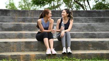 Spor elbiseli iki kadın merdivenlerde oturuyor, biri su şişesi tutuyor...