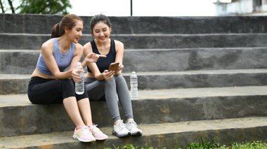 Spor elbiseli iki kadın merdivenlerde oturuyor, biri su şişesi tutuyor...