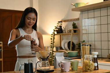 Bir kadın kahve öğütücüsünde kahve çekirdeklerini öğütüyor. Mutfak çeşitli malzemelerle dolu..