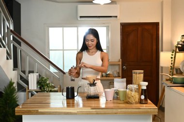 Bir kadın kahve öğütücüsünde kahve çekirdeklerini öğütüyor. Mutfak çeşitli malzemelerle dolu...