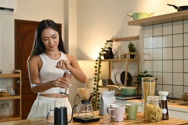 Bir kadın kahve öğütücüsünde kahve çekirdeklerini öğütüyor. Mutfak çeşitli malzemelerle dolu...