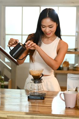 Bir kadın kahve yapıyor. Kahveyi fincana dökerken gülümsüyor..