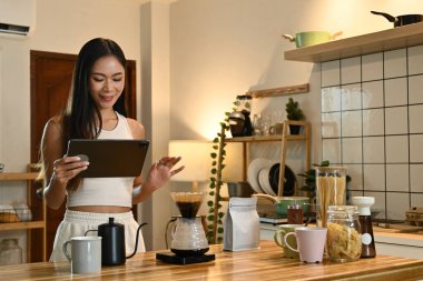 Mutfakta bir kadın tablet kullanıyor. Mutfak bardaklar, kaseler ve şişe gibi çeşitli malzemelerle donatılmıştır..