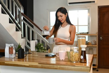 Bir kadın mutfakta kahve yapıyor. Beyaz bir atlet giyiyor ve bir fincana kahve dolduruyor..