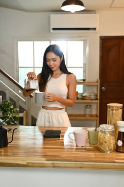 Bir kadın mutfakta kahve yapıyor. Beyaz bir atlet giyiyor ve bir fincana kahve dolduruyor...