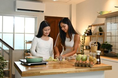 İki kadın mutfakta birlikte yemek pişiriyor. Biri sebze keserken diğeri ona bakıyor...