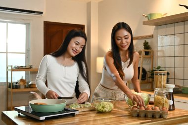 İki kadın mutfakta birlikte yemek pişiriyor. Biri sebze keserken diğeri yumurta hazırlıyor..