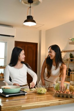 İki kadın mutfakta, yemek hazırlarken gülüyorlar ve konuşuyorlar..