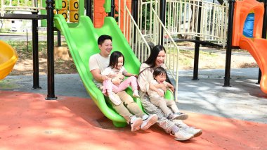 Dört kişilik bir aile parkta yeşil bir slaytta eğleniyor. Sahne mutlu ve eğlenceli, çünkü aile birlikte kaliteli zaman geçiriyor ve eğleniyor...