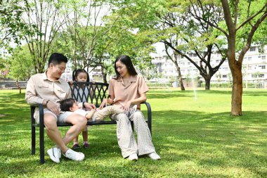 Dört kişilik bir aile parktaki bankta oturup güneşli bir günün tadını çıkarıyor. Çocuklar oyun oynuyor ve aileler onları izliyor..