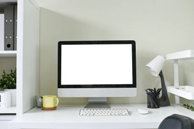 Bir bilgisayar monitörü klavye ve fareyle birlikte bir masanın üzerinde oturur. Masa temiz ve düzenli, yakınında bir fincan ve saksı bitkisi var..