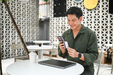 Adamın biri cep telefonu ve kredi kartıyla masada oturuyor. Telefonuna bakarken gülümsüyor...