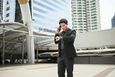 Takım elbiseli bir adam saatine bakarken cep telefonuyla konuşuyor..