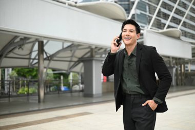 Takım elbiseli bir adam dışarıda dururken cep telefonuyla konuşuyor. Keyfi yerinde ve profesyonel olarak giyinmiş...