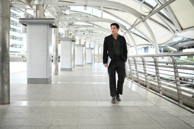 Takım elbiseli bir adam büyük, boş bir havaalanı terminalinden geçiyor. Bir evrak çantası taşıyor ve acelesi var..