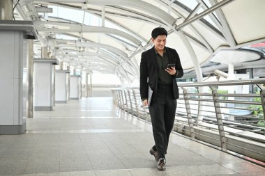 Takım elbiseli bir adam elinde cep telefonu ve diğer elinde dizüstü bilgisayarla yürüyor. Profesyonellik ve meşguliyet kavramı..