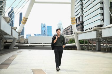 Bir adam şehir caddesinde yürüyor. Sahne, arka planda yüksek binalar olan modern bir şehirde geçiyor..