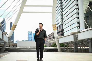 Bir adam şehir caddesinde yürüyor. Sahne, arka planda yüksek binalar olan modern bir şehirde geçiyor.