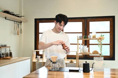 Bir adam kahve öğütücüsünde kahve çekirdeklerini öğütüyor. Kahve öğütücüsü ahşap bir masanın üzerinde...