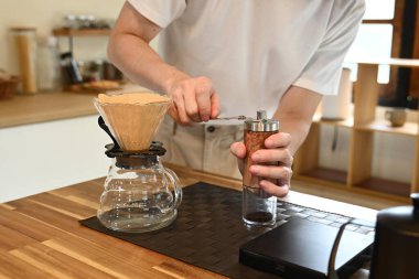 Bir adam kahve öğütücüsünde kahve çekirdeklerini öğütüyor. Kahve öğütücüsü ahşap bir masanın üzerinde..