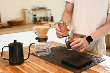 Bir adam kahve öğütücüsünde kahve çekirdeklerini öğütüyor. Kahve öğütücüsü ahşap bir masanın üzerinde..