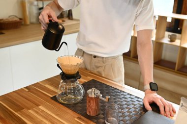 Bir adam kahve filtresine su döküyor. Kahve filtresi cam bir kabın içinde..