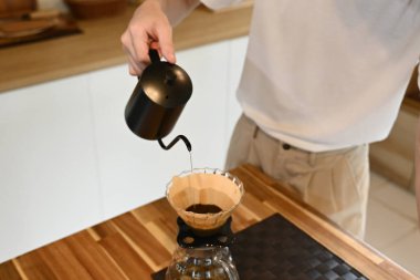 Bir adam kahve filtresine su döküyor. Kahve filtresi cam bir kabın içinde...