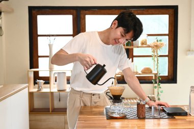 Bir adam fincana kahve dolduruyor. Kahve sade bir kahve demliğinden dökülüyor. Adam kahveyi koyarken gülümsüyor..