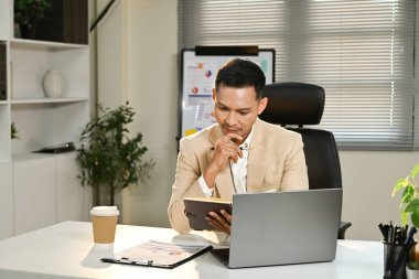 Takım elbiseli bir işadamı ofisinde dizüstü bilgisayarla bir masada oturuyor..