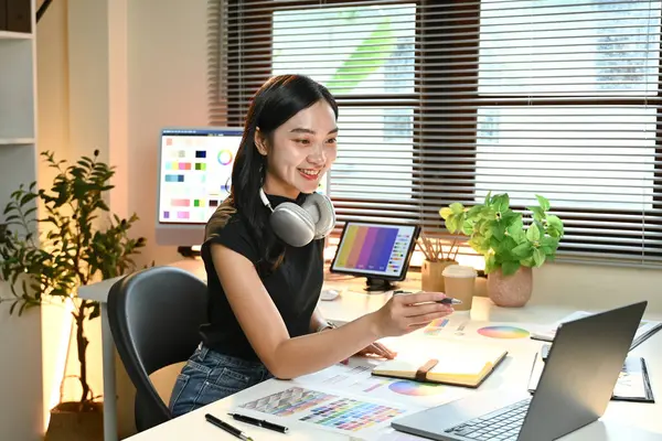 Masasında dizüstü bilgisayarı ve not defteri olan bir kadın oturuyor. Gülümsüyor ve mutlu. Masa bir saksı bitkisi, bir klavye ve bir fare gibi çeşitli eşyalarla dolu.