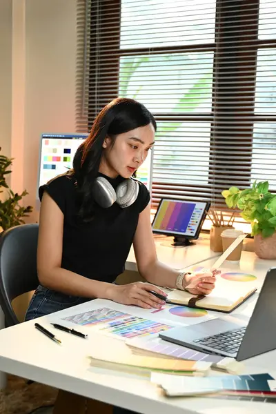 Masasında dizüstü bilgisayarı ve not defteri olan bir kadın oturuyor. Bir proje üzerinde çalışıyor ve odaklanmış durumda.