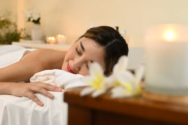 Beyaz bornozlu bir kadın masaj masasında yatıyor. Gülümsüyor ve rahatladı..