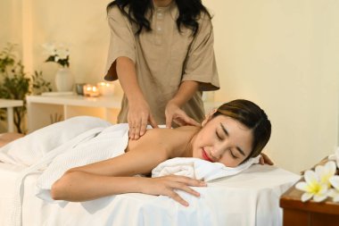 Bir kadın masaj terapistinden masaj alıyor. Gülümsüyor ve rahatlıyor. Masaj masası beyaz bir havluyla kaplı..