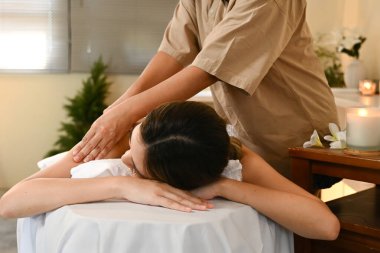 Bir kadın masaj terapistinden masaj yaptırıyor. Kadın gülümsüyor ve masajın tadını çıkarıyor. Oda loş bir şekilde aydınlatılmış ve yakınlardaki bir masada mumlar var..