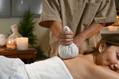 Profesyonel masör, dingin spa ortamındaki kadınlara sıcak bitkisel top tedavisi uyguluyor. Rahatlamayı ve sağIığı destekliyor..