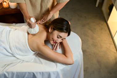 Profesyonel masör, dingin spa ortamındaki kadınlara sıcak bitkisel top tedavisi uyguluyor. Rahatlamayı ve sağIığı destekliyor..