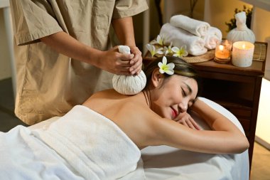 Derin rahatlama için sıcak bitkisel top ile vücut masajı. Spa salonunda masaj yaptıran bir kadın..