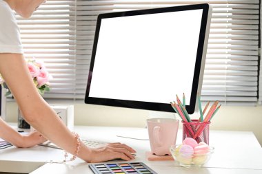 Bir kadın bilgisayar monitörü ve bir fincan kahveyle masada oturuyor. Monitör boş ve kadın klavyede yazı yazıyor..