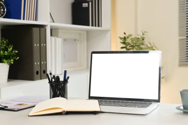 Bir dizüstü bilgisayar bir defter ve bir fincan kahveyle bir masanın üzerinde oturur. Dizüstü bilgisayar boş bir ekrana açık.