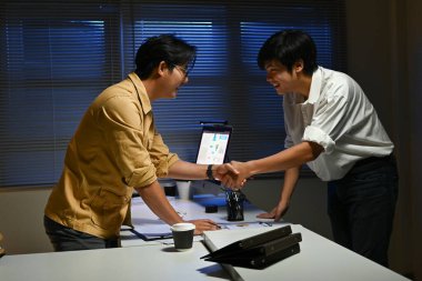 Loş bir odada el sıkışan iki adam. İçlerinden biri gözlük takıyor. Sahne profesyonel ve dostane.